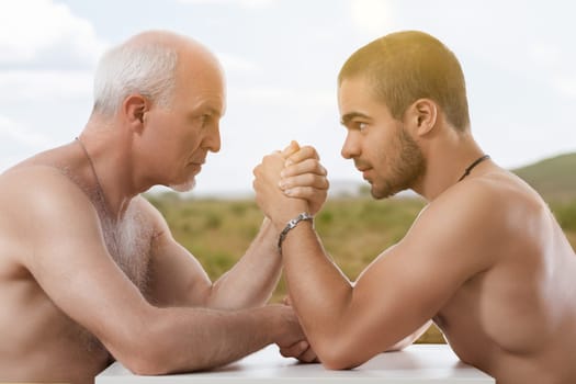 Intense arm wrestling match between elder and younger bare-chested men