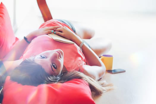 Reversed shot of young woman lying with a notebook on her belly and idyllic 1970s lighting overlays, she has long brown hair and looks into the camera