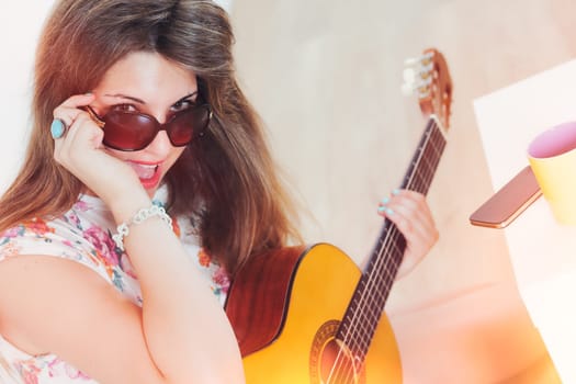 Girl with sunglasses used to be a fashionable chick, at a party or in her room plays or pretends to play classical guitar like a pop star.