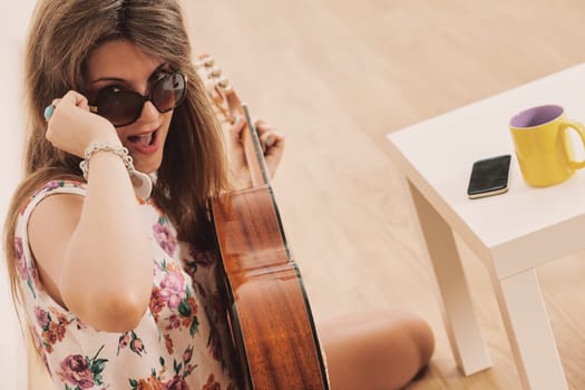 Girl with sunglasses used to be a fashionable chick, at a party or in her room plays or pretends to play classical guitar like a pop star.
