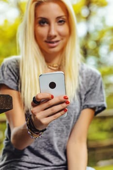 Beautiful blond girl in an outdoor forest or public park on a sunny day. She has very visible braces that make her even prettier. She is out of focus but the smartphone in the foreground is in focus