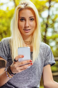 Beautiful blond girl in an outdoor forest or public park on a sunny day. She has very visible braces that make her even prettier. She has a smartphone that she has stopped looking at to turn her atten