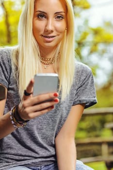 Beautiful blond girl in an outdoor forest or public park on a sunny day. She has very visible braces that make her even prettier. She has a smartphone that she has stopped looking at to turn her atten