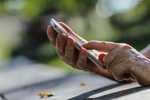 On rugged park wood, a senior's fingers wrestle with a phone. Today's tech, being small and sensitive, pushes the aged towards social isolation