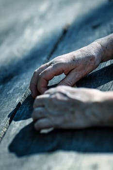 The hands of an old woman, etched by time's tale, rest amidst nature's backdrop in a forest. Their appearance tells of a lifetime's journey, replete with challenges and feelings