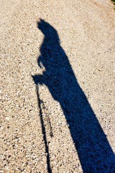 The sunset casts the outline of an aged woman on the ground, symbolizing the evening phase of her life Weary yet hopeful, she clutches her stick, looking skyward