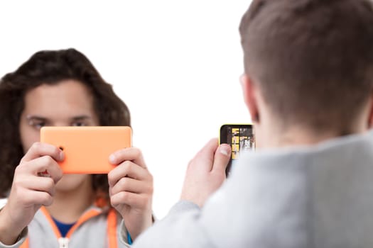 Two boys stand in front of each other. Each of them is focused on staring at their smartphone screen while facing another human being.