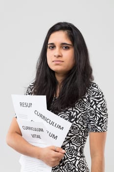 Half-length portrait of newly graduated Indian student clutching to herself all the resumes she has prepared and is sending everywhere. It's not easy but she tries hard.
