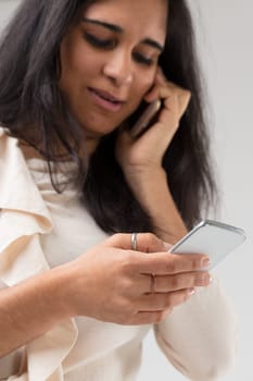 Focus on the hand of a young Indian woman (blurred) clutching a smartphone on which she is scrolling, while with the other she holds another to her ear with which she listens and talks.