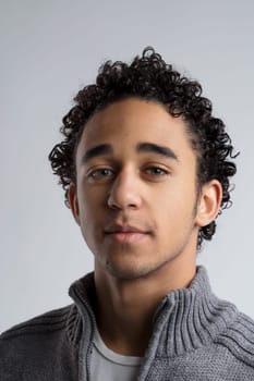 Captured against a neutral backdrop, a young man with curly dark hair exudes a sense of contemplation, his green eyes hinting at a story