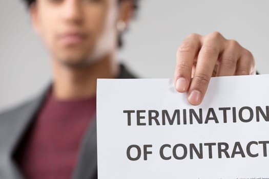 Amidst muted emotions on a blurred face, the starkness of a termination notice resonates, emphasizing the gravity of the situation