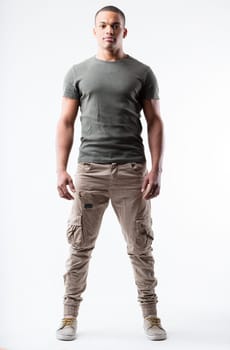 Fit young black man, V-shaped chest, lean waist in a relaxed yet strong pose. Very short hair, military-inspired outfit, low sneakers, slight smile. Full frontal portrait, isolated from background