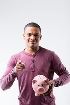 A black man pointing at us, holding a piggy bank. He urges us to save for investing or purchasing. Advocating against squandering money, he's in a burgundy shirt, white background