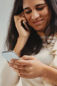 Focused on foreground phone, blurred woman listening to a second smartphone in the background. Engrossed in her phone conversation, she balances another device, symbolizing today's interconnected lif