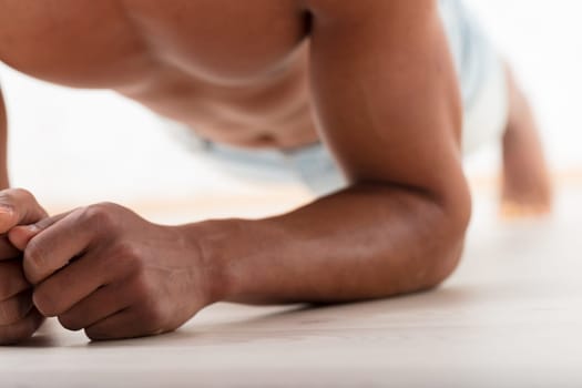Unrecognizable black man holds a stoic plank, elbows grounded. His evident pectorals and abs show his commitment to exercise for attractiveness and long-term health