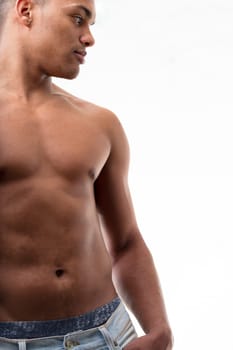 A fit young man, shirtless, gazes sideways. His undergarments visible beneath his trousers, his thumb casually hooked into a pocket. His chest and abs in view, skin glistening, isolated from the backg