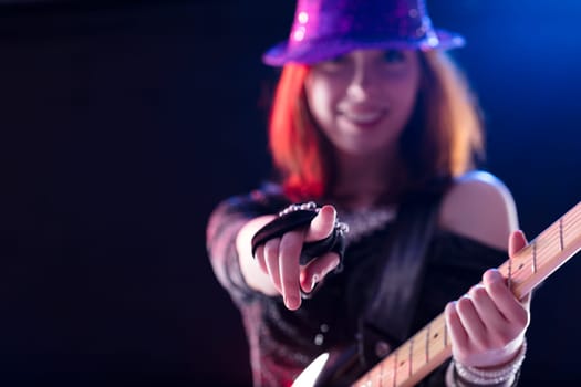Exuberant female guitarist in a glittery purple hat points confidently during a vibrant performance