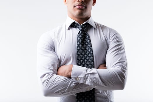 Businessman of black ethnicity, partially visible face, stands arms crossed, exuding strength and steadfastness. In white shirt, dark patterned tie. Muscular, white background