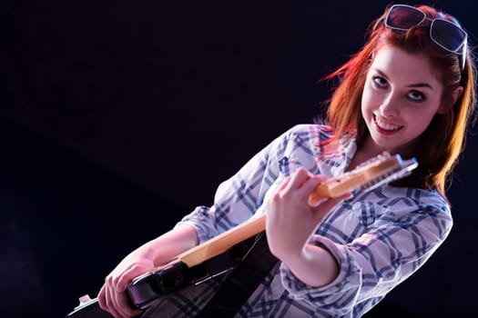 Red-headed musician in casual attire shares a charming smile, holding her guitar with ease