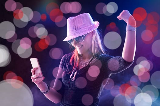 Enthusiastic woman with phone celebrates, her attire and pose matching the party's sparkle