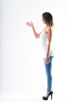 Caught mid-conversation, a young woman gestures with her arm. Full-length portrait of a tall, slim woman in skinny jeans, high heels, and a shoulder-revealing tube top. White background