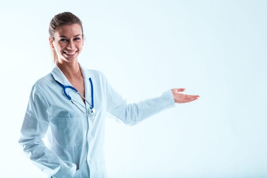 Enthusiastically smiling doctor indicating something in the air. An expert in medicine in a tidy white coat, knowledgeable and attractive. She's pointing to the product next to her in the copyspace