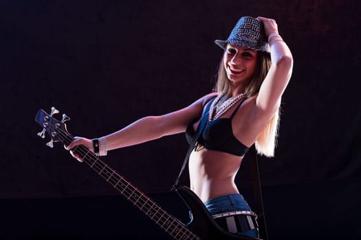Sexy pop-rock star playing bass guitar with energy. Dressed in high heels, skinny jeans, black bra, and glimmering belts, she moves with confidence, showcasing her toned abs
