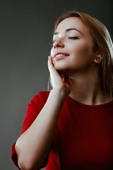 Woman in red exudes joy with a closed-eye smile, hand gently on her neck in a concept of skin care and purity.