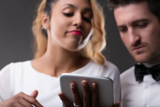 Black woman engrossed in digital tablet man covertly observes, a furrow of concern visible