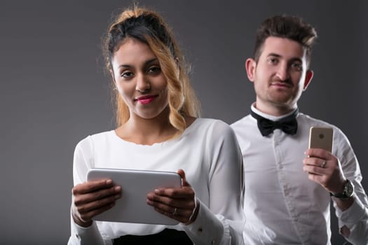 Young black woman holds a tablet, white man with phone in background