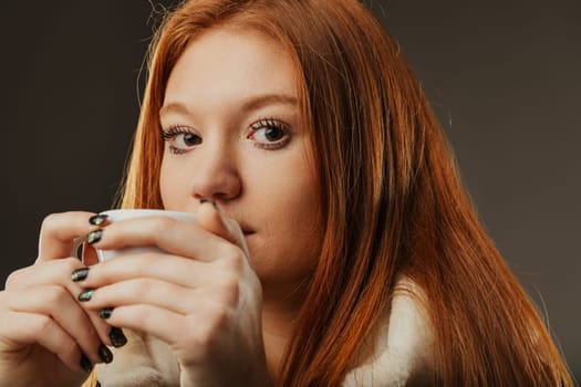 Auburn-haired woman enjoys a warm beverage, her eyes inviting a shared moment
