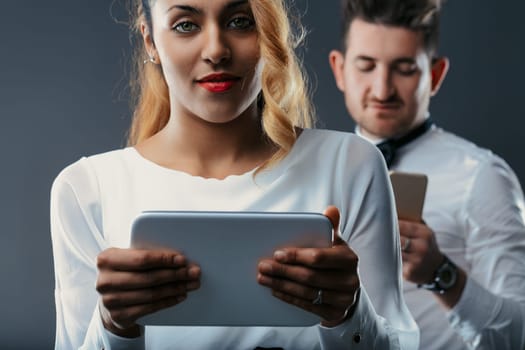 She commands the foreground with a digital slate, while he is partially hidden, engrossed in his device