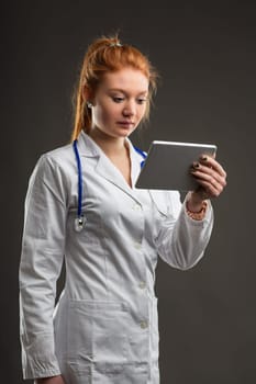Medical professional consults digital device, her red hair reflecting a unique identity in healthcare