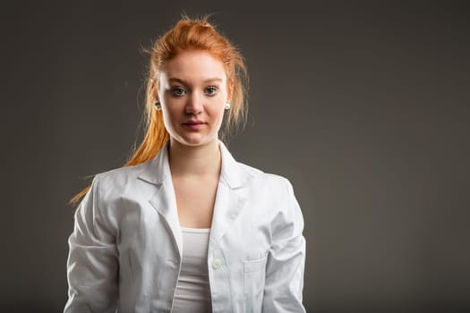 Technical specialist in a lab coat stands with determination, her red hair marking a bold presence in a field of precision