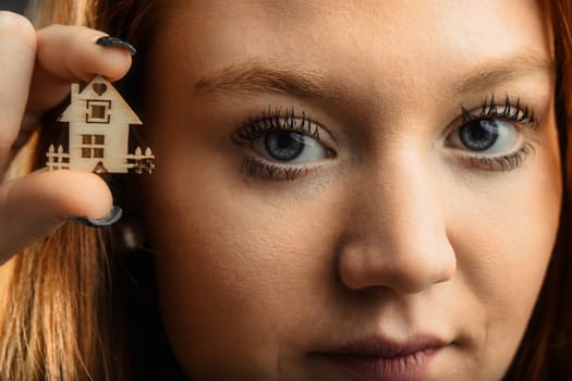 Woman with auburn hair presents a tiny wooden house, symbolizing aspirations