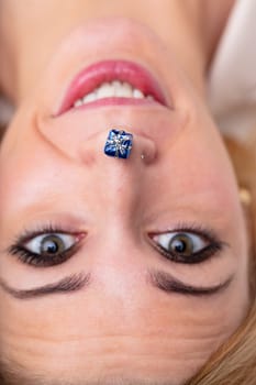 Ultra-close portrait of surprised woman, upside-down, mini-gift on nose. Symbolizes gifts, holiday celebrations