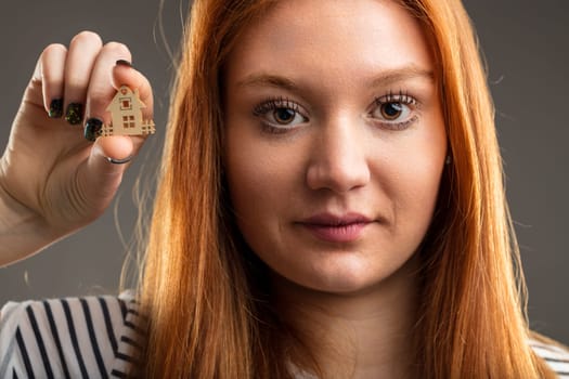Redhead holds a miniature house, her expression reflecting dreams of home
