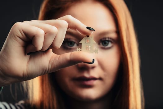 Intense gaze of a woman grasping a model house, evoking thoughts of stability