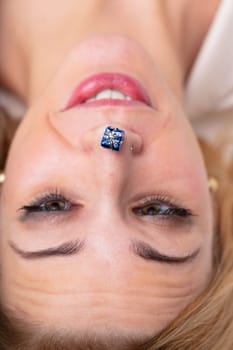 Upside-down face of joyful woman with a tiny gift on her nose. Idea of gifts, Christmas, festivities, celebrations