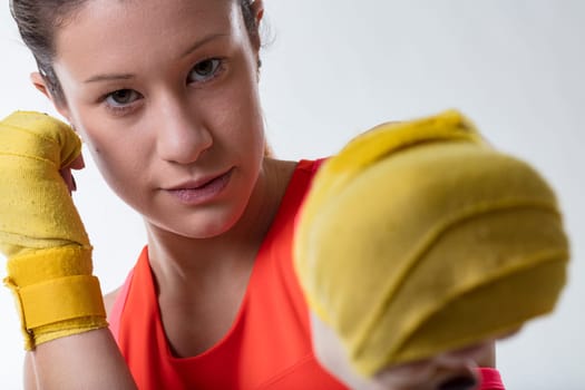 Female sport-fighter in a guard stance, her eyes locked on target, punches in her orange top and bandaged hands
