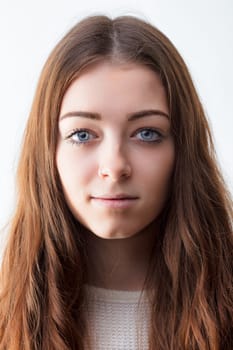 Young woman with clear skin and a neutral expression stands against a white backdrop, her long brown hair framing her face