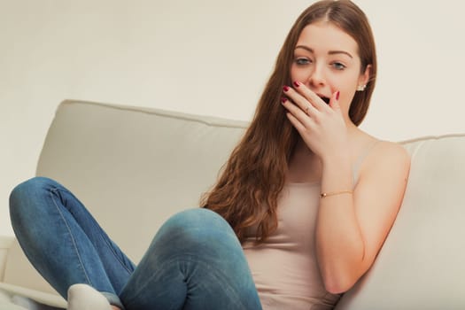 The young woman's casual pose on the couch, paired with a stifled yawn, captures the essence of a lazy afternoon