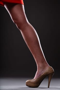 Female leg in action from a red skirt forms a diagonal, highlighted by a moderately high heel, offering classic femininity. Sophisticated grey-black background