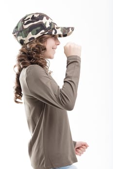 Smiling girl in military green, camouflage cap, and jeans, dances joyfully. Her long curls sway with her ballet-like movements on white backdrop