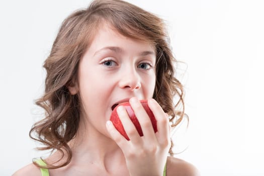 A curly-haired girl in a green tank top bites into a juicy red apple, symbolizing healthy habits