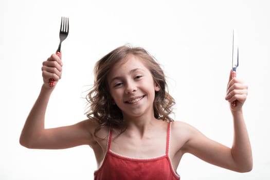 A little girl in a red tank top eagerly holding a fork and knife, awaits her meal with joyful anticipation