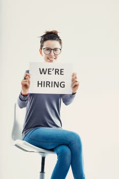 The cheerful individual holds a 'We're Hiring' sign, her bright smile reflecting the welcoming nature of the business