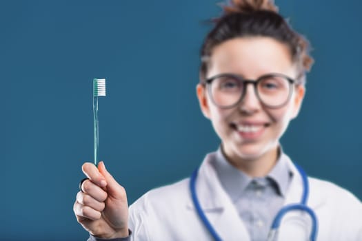 Smiling dentist foregrounds a clear toothbrush, emphasizing the importance of dental care
