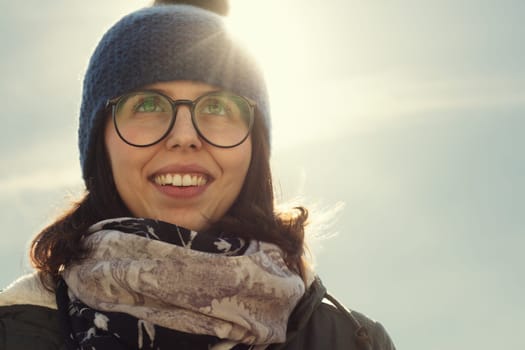 The sun's glare adds a dreamy quality to the woman's blissful smile, wrapped in winter fashion