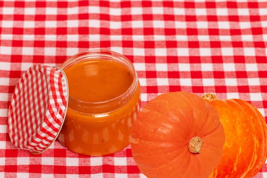 Natural cosmetics. Selective focus on a homemade pumpkin face mask in a glass jar and pumpkins on red checkered napkin. DIY cosmetics and SPA. Copy space.